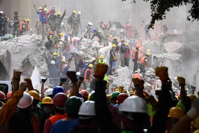 Personas y brigadistas levantan los brazos frente a una estructura colapsada